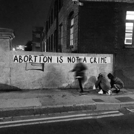 Women graffitiing a wall with the slogan "abortion is not a crime"