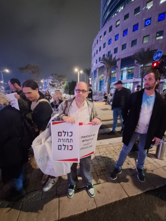 Adam Keller holding signs that say "No to war - Yes to peace" and the other one says "All for All" (i.e. all Palestinian prisoners in Israeli prisons in exchange for all captive Israelis in Gaza). 