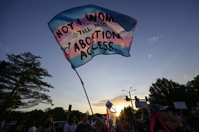 Trans flag with the words stitched on: "Not a woman/Still need abortion access"