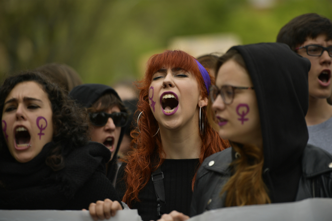 Three women at a protest in Spain, with the feminist symbol painted on their cheeks