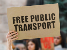 A hand holding a placard which reads "Free Public Transport".