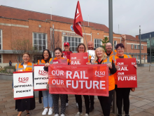 Photograph shows a TSSA picket line at Doncaster station; pickets in orange hi-vis vests hold up red placards and banners reading "Our Rail, Our Future"