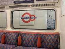 Photo shows the inside of a Bakerloo line train, with the station roundel for Wembley Central and a "no smoking" sign visible in the window