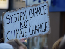 A hand holding a placard which reads "System Change not Climate Change"