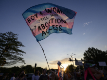 Trans flag with the words stitched on: "Not a woman/Still need abortion access"