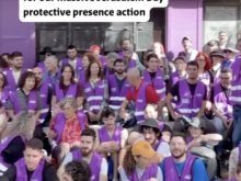 A large group of people wearing purple high-visibility vests, many seated and others standing, gathered outside a purple building. A white text overlay reads: “Just half the number of Solidarity Guard activists in Jerusalem right now for our massive Jerusalem Day protective presence action.”