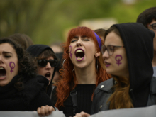Three women at a protest in Spain, with the feminist symbol painted on their cheeks
