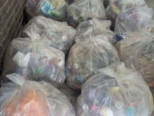 A large pile of clear plastic bags filled with rubbish stacked along the wall of a London Underground station concourse, with passengers walking in the background.