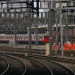 Railway junction with multiple electrified tracks, a London Underground train in the background, and a group of railway workers in orange high-visibility clothing walking beside the tracks.