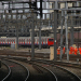 Railway junction with multiple electrified tracks, a London Underground train in the background, and a group of railway workers in orange high-visibility clothing walking beside the tracks.